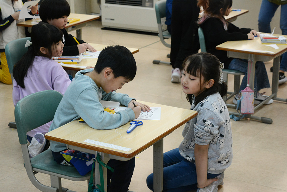 協力して「くるくるヘビ」を作る１年生と子どもたち